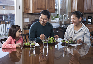 Hombre, mujer y niña comiendo una comida saludable en su casa.